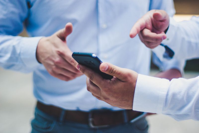 A man showing and pointing to a cell phone to another person.