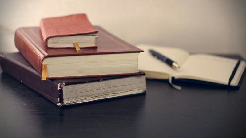 A stack of three books with a notebook and pen, symbolizing traditional writing.