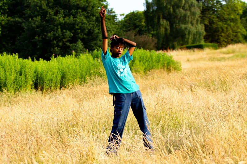 A person in makeup, t-shirt and jeans standing in a prairie field.