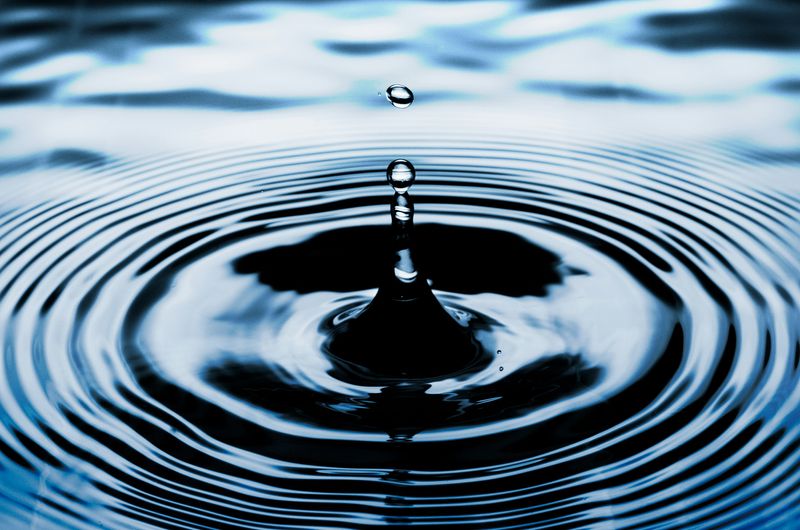 A droplet landing in a pool of water, creating ripple waves.