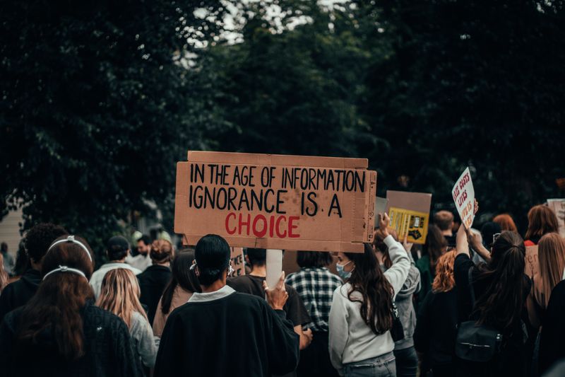 A sign at a protest. It reads: in the age of information, ignorance is a choice.