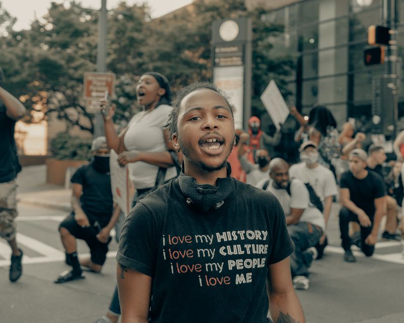 A young black man at a rally. His shirt reads,