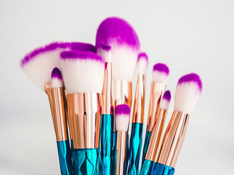  A set of makeup brushes with metallic blue handles white bristles tipped in purple.