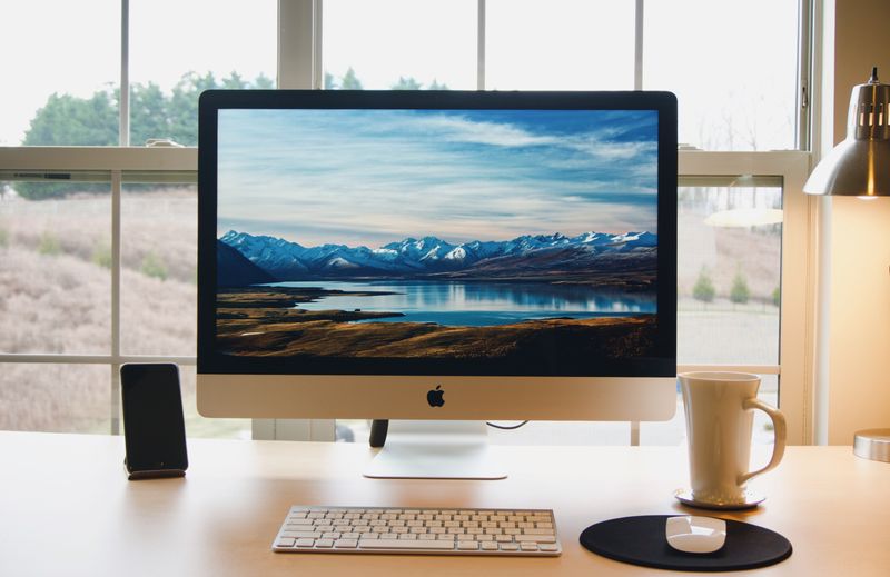 A Mac monitor on a desk showing a mountain background