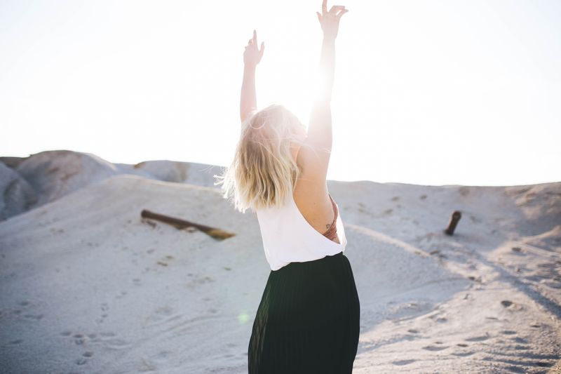 Woman outside enjoying the sunlight with her arms raised