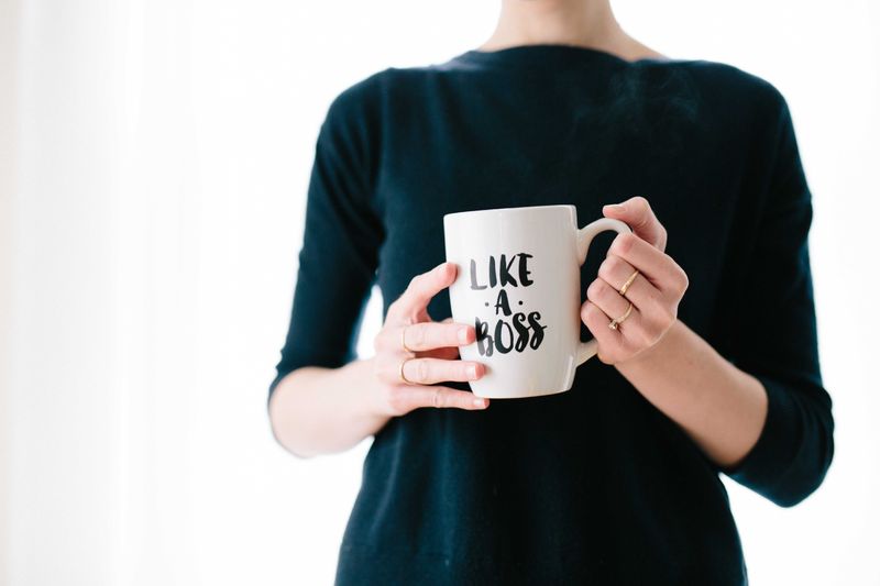 Image is zoomed in on a person's torso. They are wearing a green shirt and holding a mug that says 'Like A Boss.'