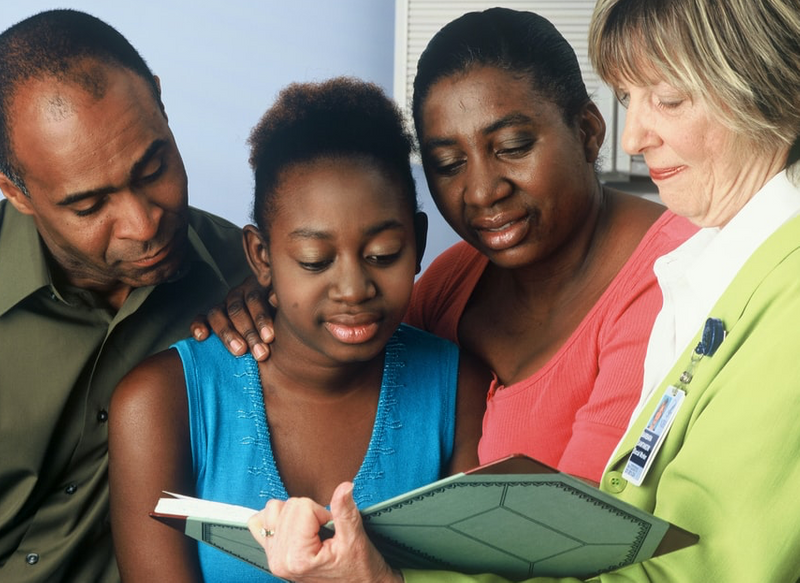 A man and woman sitting with a teenage girl looking at an open book being held by a woman of another race.