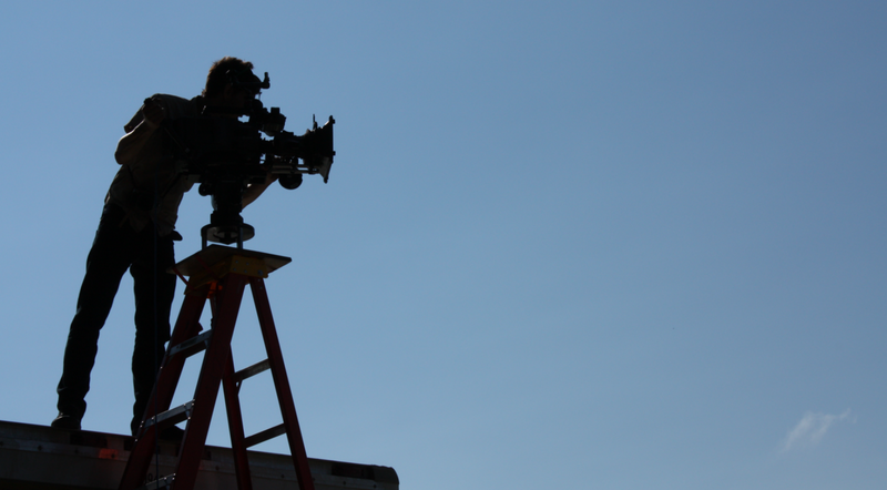 Director of Photography in silhouette standing on a box truck with camera mounted on top of a ladder.