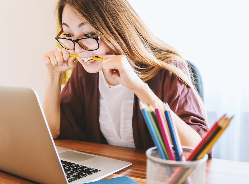 Woman looking at laptop biting on pencil out of anxiety.