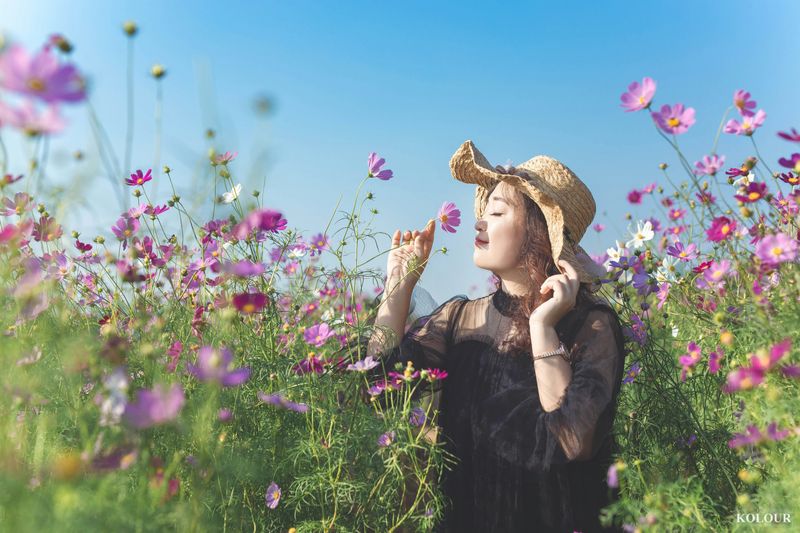 A woman standing in a field and smelling a flower.