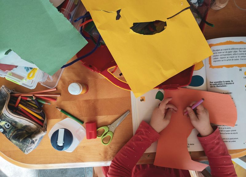 A child engaged in arts and crafts. Colored pencils and construction paper on a desk as the student creates artwork. 