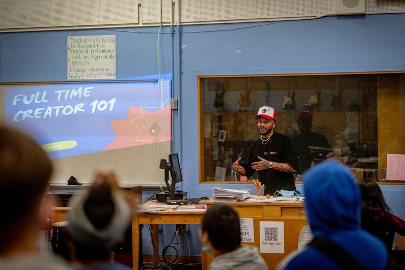 a man in a black shirt and white and red hat, teaching students in a classroom