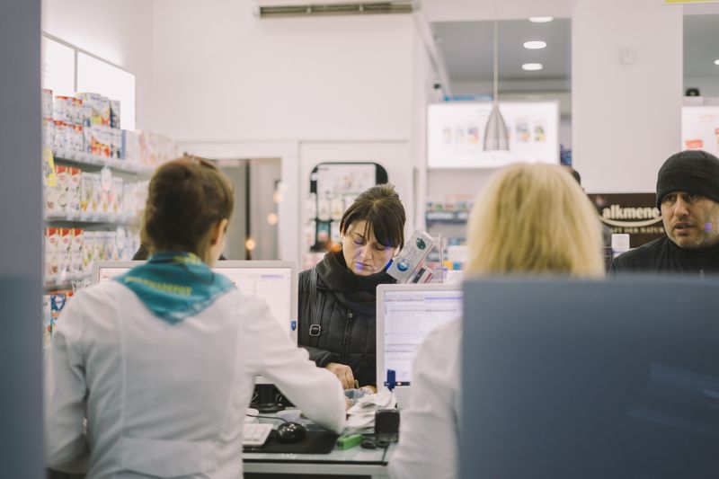 Image of a pharmacy counter. A pharmacist is giving out medication to a customer.