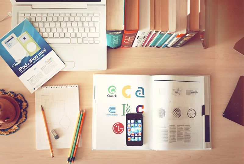 A desk with a logo design book, pencils, and a laptop.