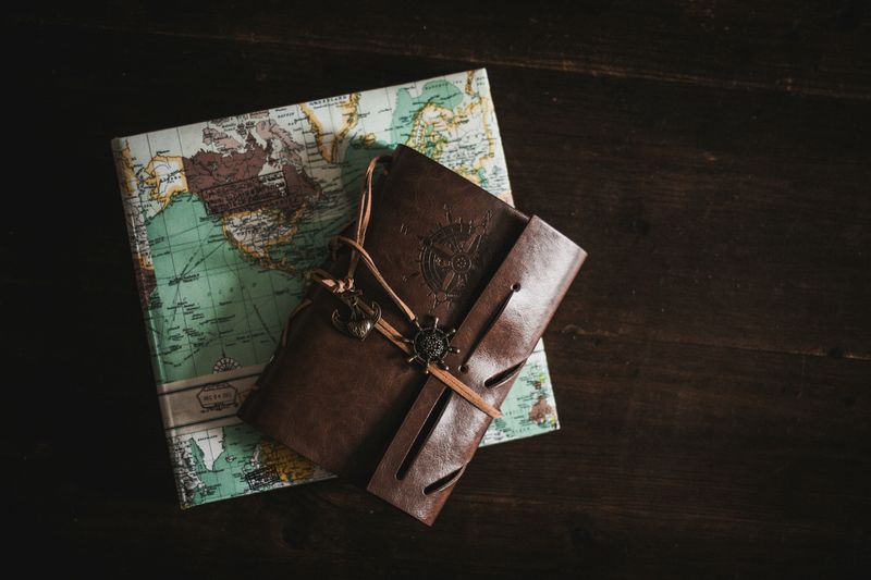 brown leather bound journal with a compass engraving laying on top of a map book