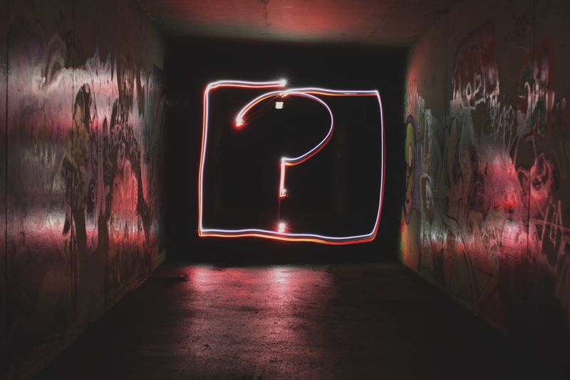 Question mark in neon lights on a wall in a dark industrial space