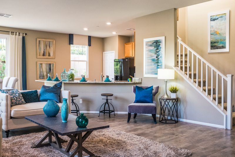 A brightly lit living room with blue accent pillows and vases and stairs to the right.