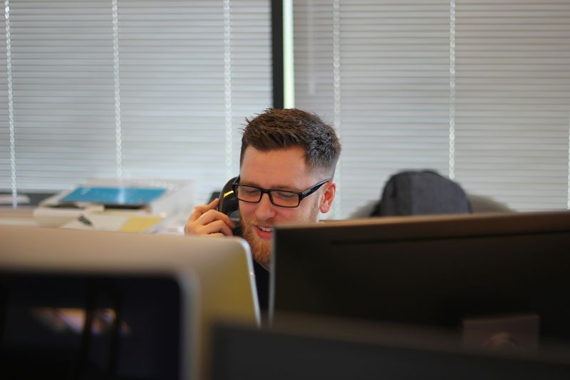 A man sitting at an office desk while talking on the phone.