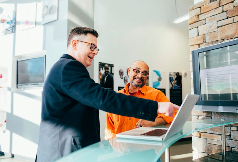 A salesperson pointing to a laptop screen while speaking with a customer.