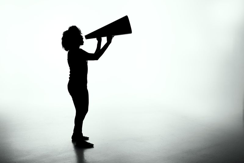 Black silhouette of person holding megaphone to mouth against white background