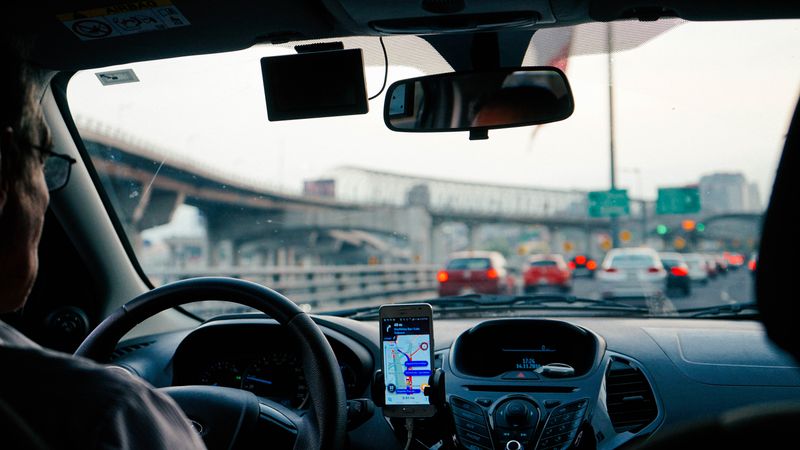 An elderly man is sitting in a car stuck in traffic. He can see the highway signs ahead of him.