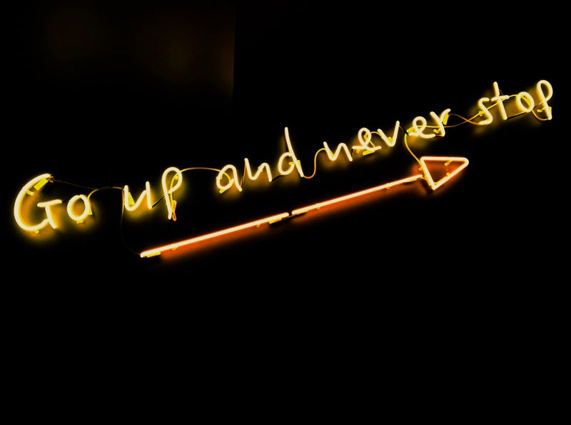 A neon sign that says, 'Go up and never stop' with an arrow pointing upwards