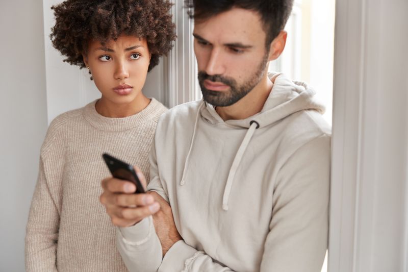 A boyfriend looks at his phone while girlfriend looks concerned.