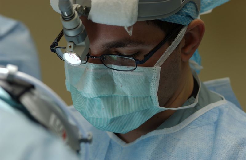 Male surgeon with surgical headlight wearing glasses and face mask.