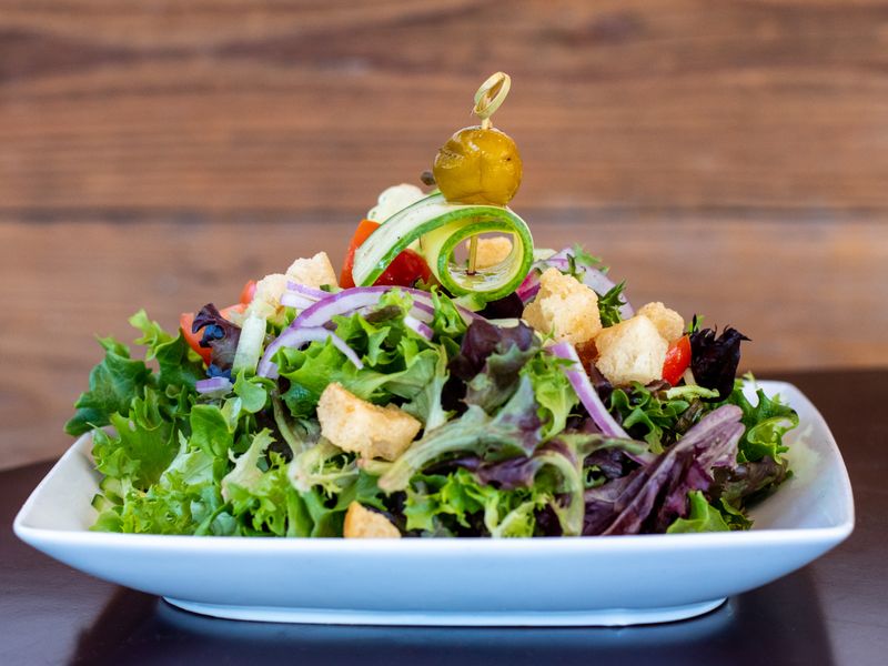 A fresh green salad topped with golden croutons, tomatoes, and a rolled piece of zucchini on top. 