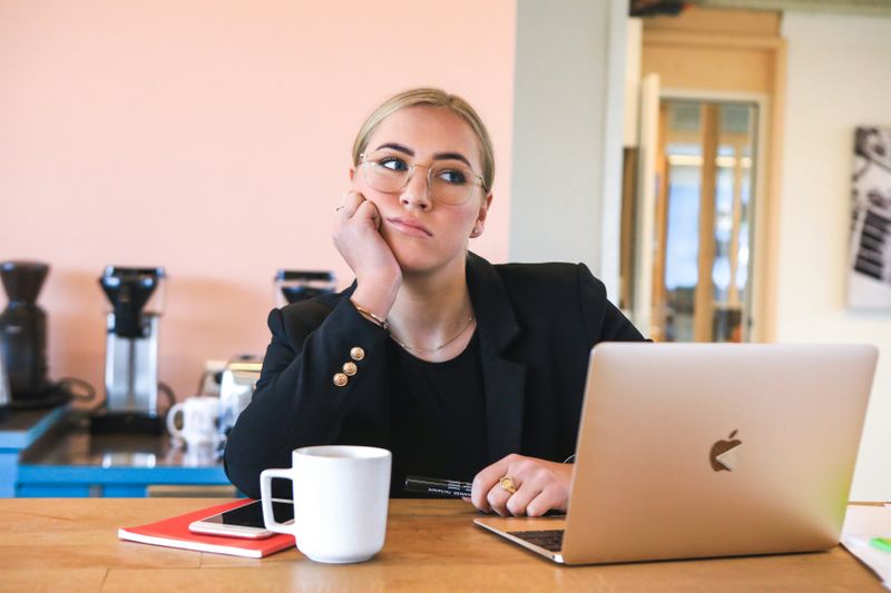 A woman sitting and thinking at a desk in front of a computer.