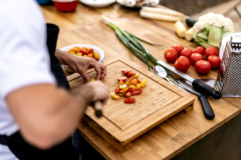 A person in a kitchen chopping tomatoes on a wooden cutting board.