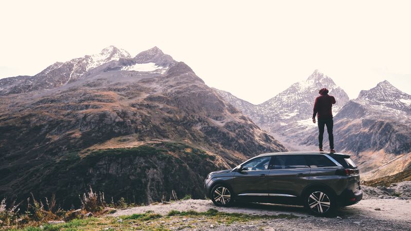 A person standing on an SUV, admiring a mountain peak.