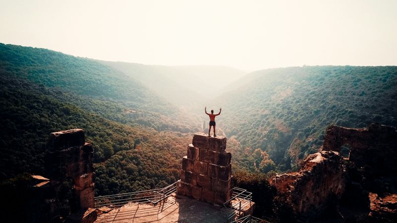 A man stands on top of a stone wall overlooking hills.