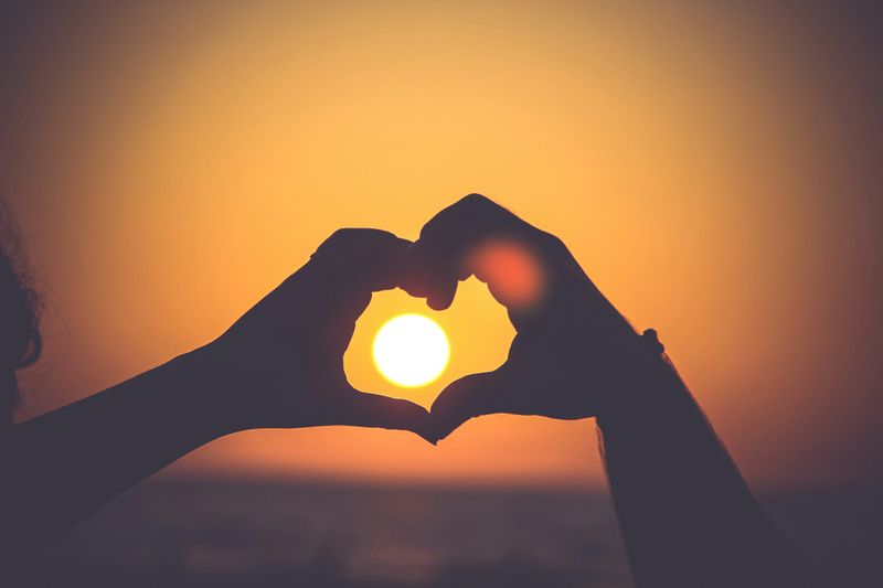 Two hands forming a heart over the sky. A setting sun appears in the heart.