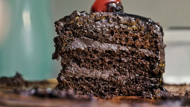 A very moist piece of chocolate cake with 3 layers and a cherry on top.