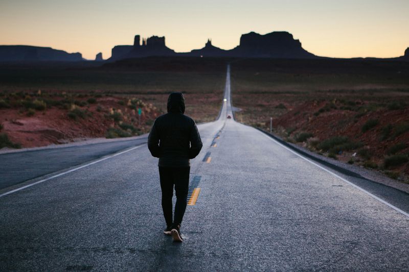 A person running down a long, straight and empty desert road at dusk. 