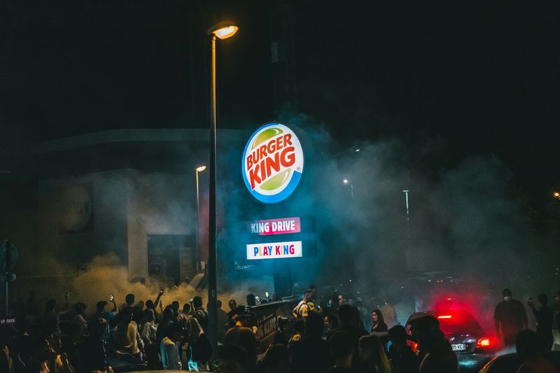 The original Burger King logo on a sign in a parking lot. A crowd gathers around it.