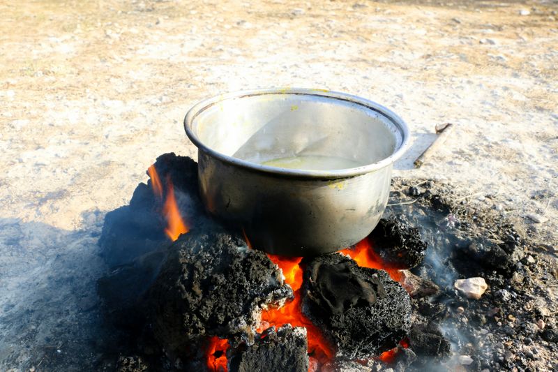 A metal pot on red, flaming coals. Smoke blows away from the coals.