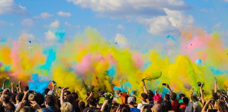 People celebrating Holi. A large crowd, hands in the air, with colorful puffs above them.