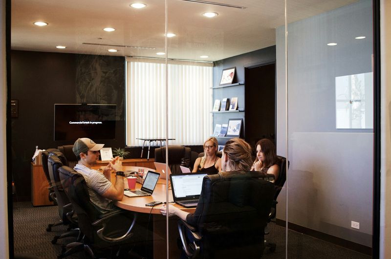 Four people sitting in chairs in a conference room on their laptops.