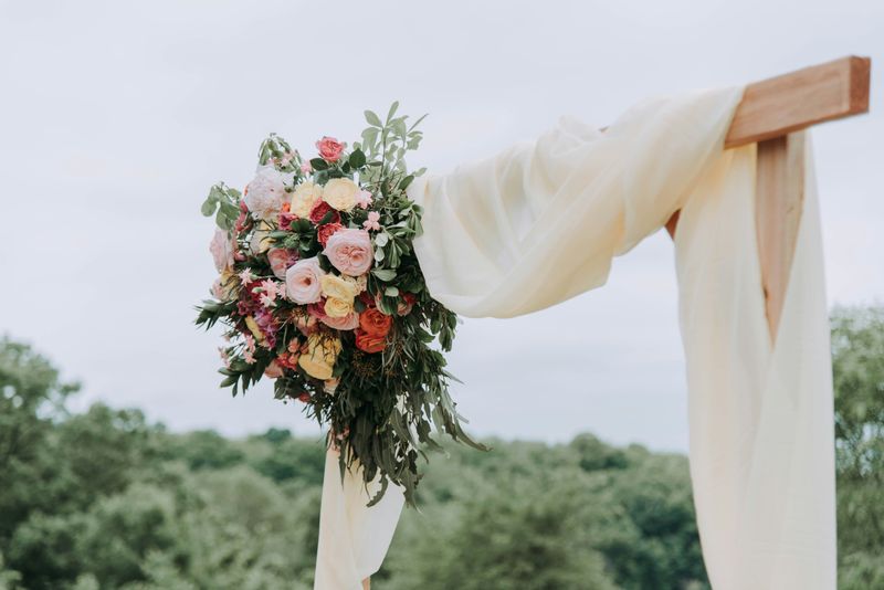 A wedding arch with flowers in the corner and a white curtain draped over it. 