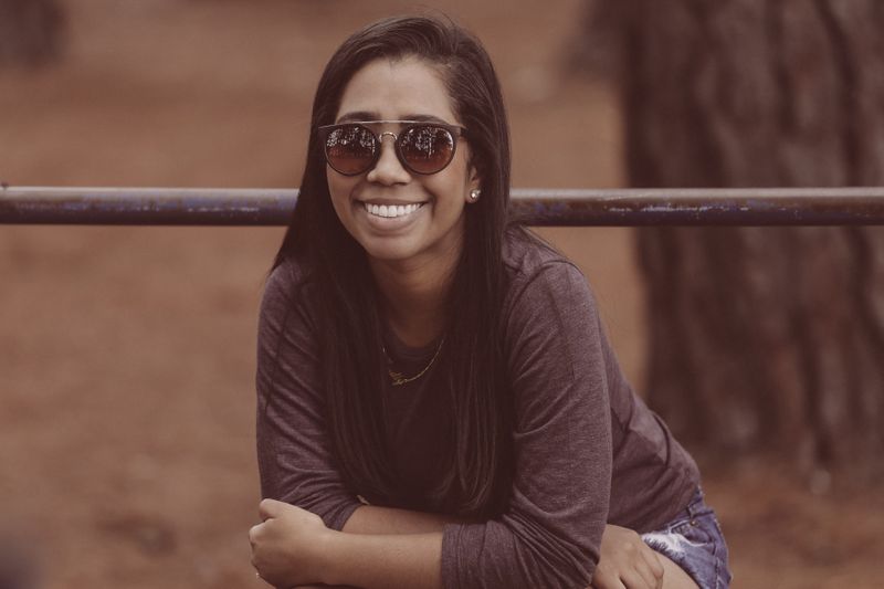 a woman wearing a maroon long sleeved shirt squatting in front of a tree and a brown background