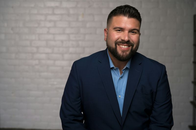 A man with short hair and a beard smiling and wearing a business suit in an office.