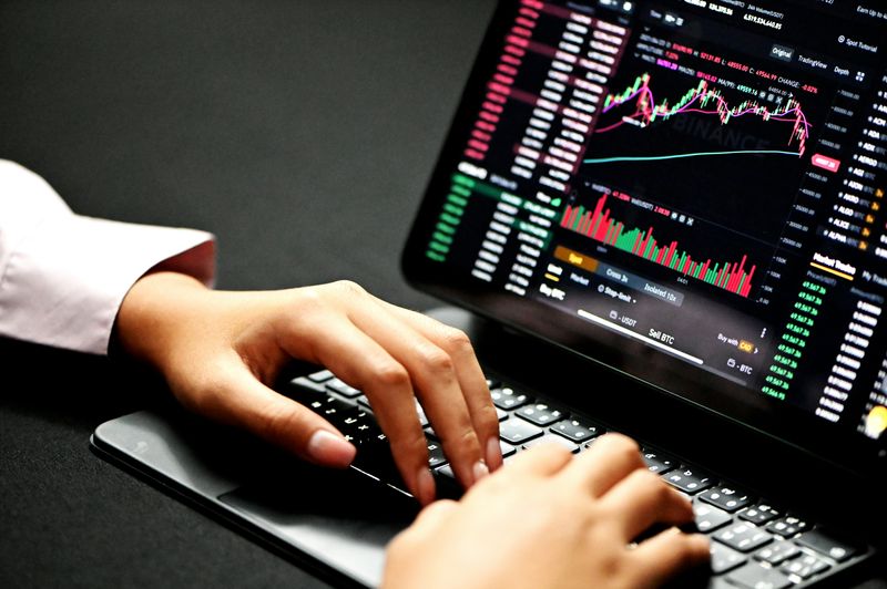 A person looks at the stock market graphs rising and falling on a laptop.