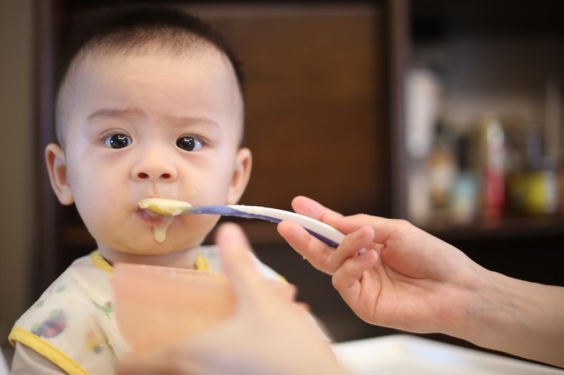 An adult feeds soft baby food to an older infant.