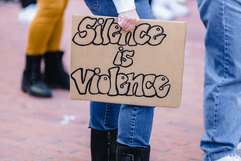 A women holding a protest sign that reads, 'Silence is violence'.