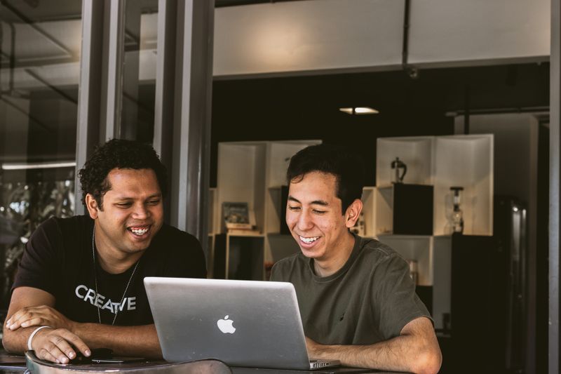 Two men sitting next to each other working on a laptop and smiling