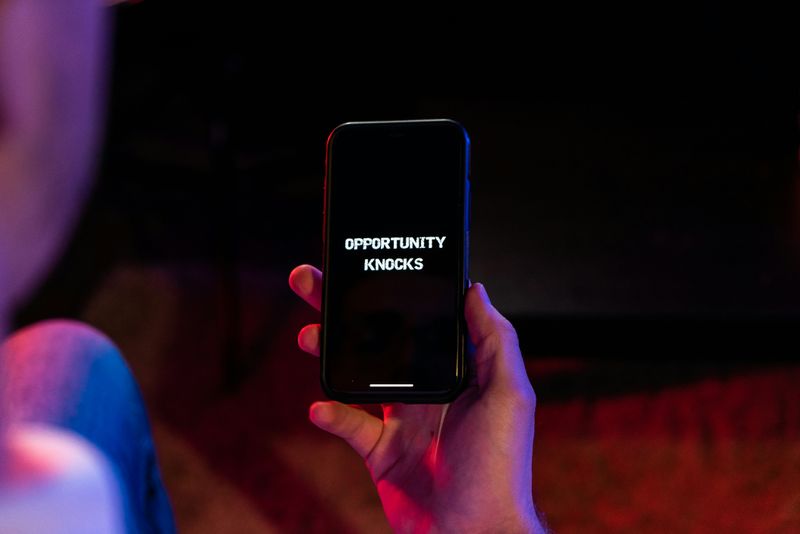 A person holding a cellphone. The text on the screen reads: 'Opportunity knocks'.