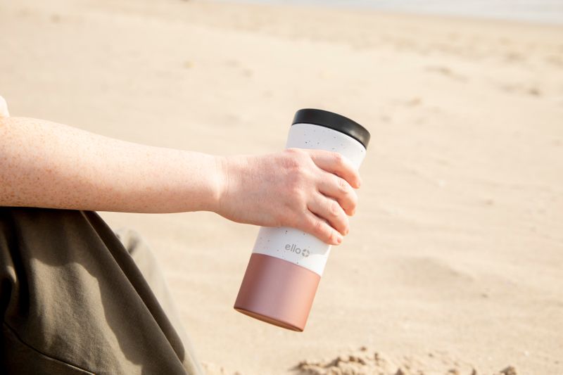 A person holding a travel mug over a sandy background