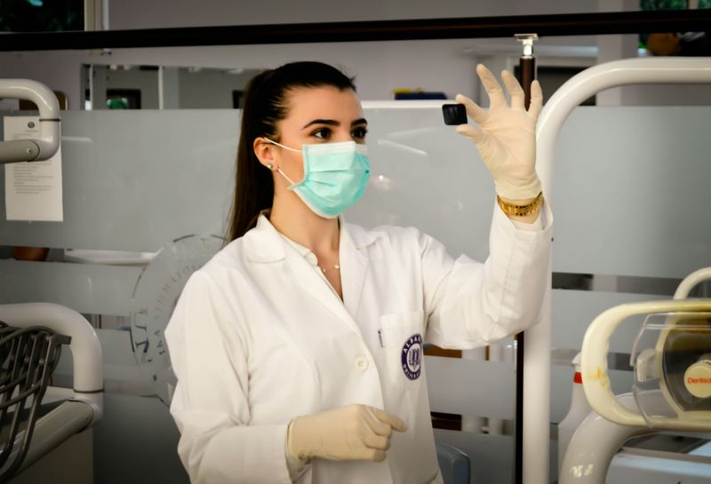 A female lab tech wearing a mask and gloves examining a sample in a medical lab.